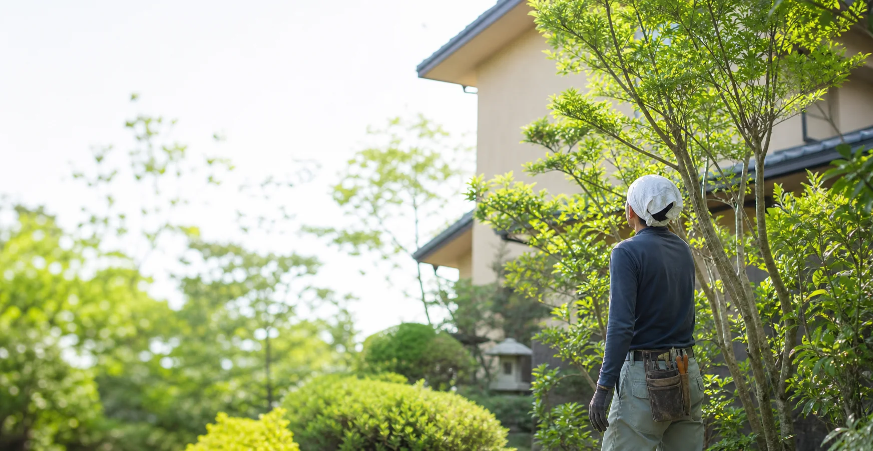 住宅の庭で庭木の状態を確認する職人